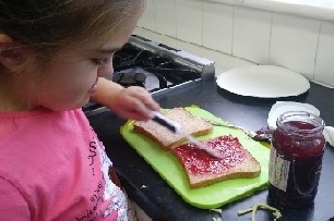 Girl in pink top spreading jam on a slice of bread